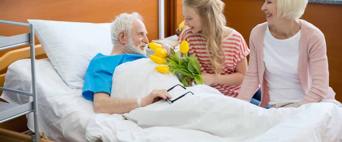 grandmother and granddaughter with tulip flowers visiting patient in hospital. male patient in