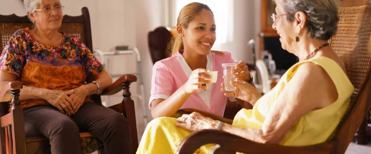 Hospice Nurse Serving Pill Medicine Water To Old Woman